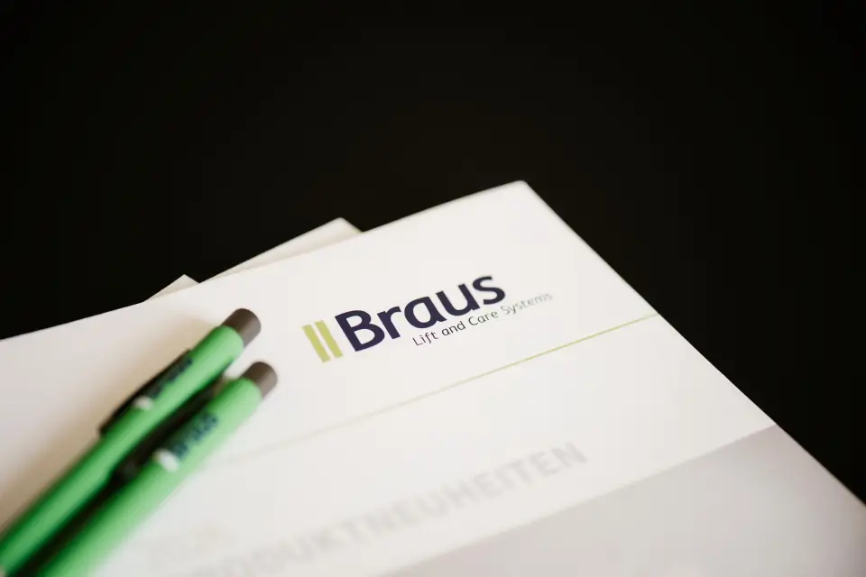 Braus-Broschüre mit zwei Kugelschreibern auf einem dunklen Tisch