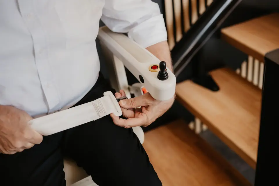 Nutzer legt am Treppenlift den Sicherheitsgurt an, an der Armlehne der Joystick