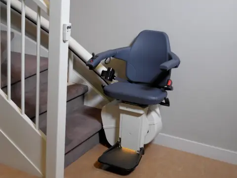 Treppenlift mit grauem Sitz an einer geraden, mit Teppich belegten Treppe