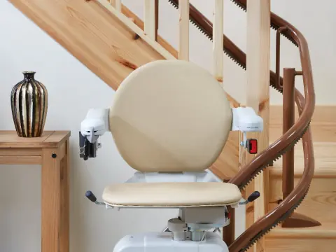 Treppenlift mit beigem Sitz an einer Holztreppe mit Kurve