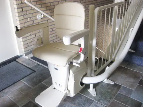 Treppenlift mit hellem Sitz und Kurvenschiene in einem Treppenhaus mit Klinkerwand
