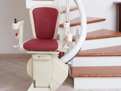 Treppenlift mit rotem Sitz an einer gewendelten Marmortreppe