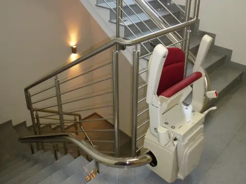 Treppenlift mit rotem Sitz in einem Treppenhaus mit Edelstahlgeländer